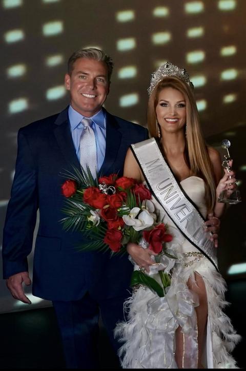 Kellie Lightbourn, crowned, in her sash with roses and trophy, beside a man in a navy suit