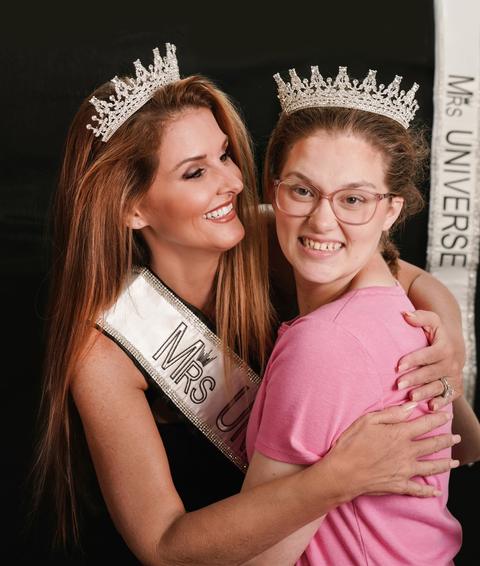 Kellie Lightbourn in her sash sharing a warm embrace with a young woman in a tiara