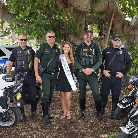 Kellie Lightbourn in her sash with four law enforcement officers beside their motorcycles