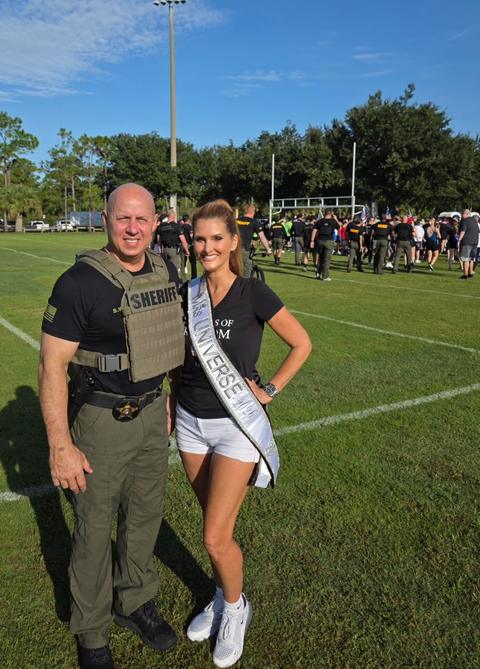 Kellie Lightbourn in her sash with a sheriff’s officer at an outdoor field event