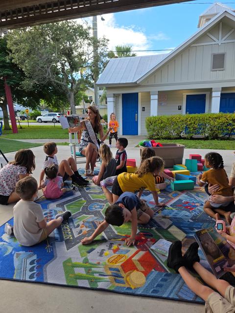 Kellie Lightbourn reading aloud to a group of children on a rug under a pavilion