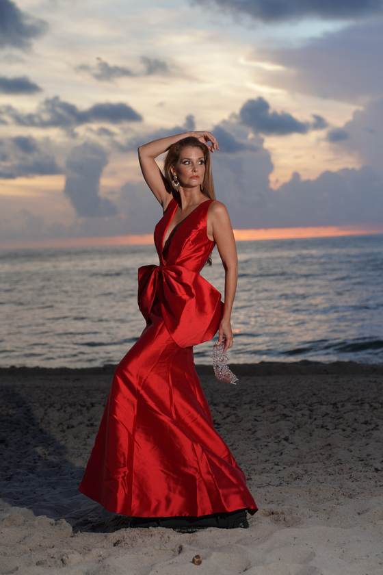 Kellie Lightbourn, Mrs. Universe® 2026, in a red bow gown at sunset, arm raised, holding the crown