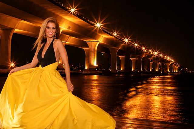 Kellie Lightbourn, Mrs. Universe® 2026, twirling in a yellow gown beneath a lit bridge at night
