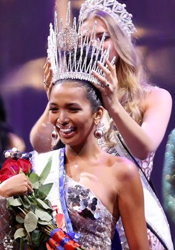A titleholder being crowned on stage, holding roses