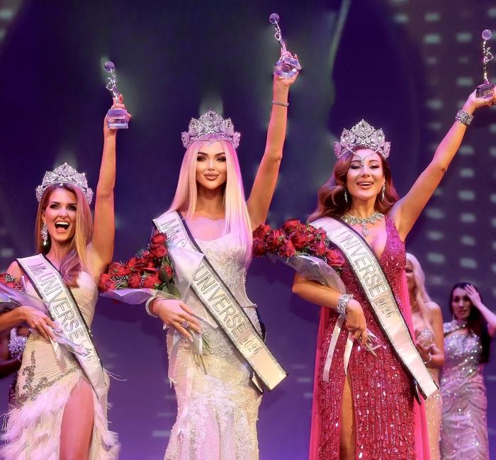 Kellie Lightbourn, in the white feathered gown, celebrating with two fellow crowned winners on stage