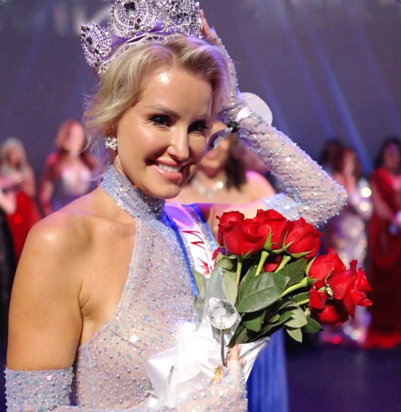 A newly crowned titleholder smiling on stage with red roses