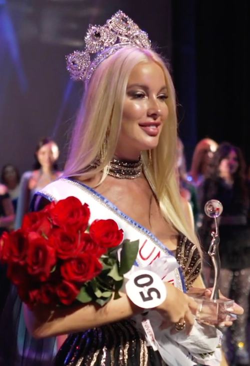 A crowned titleholder holding red roses on stage